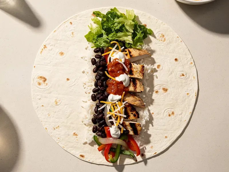 Step 8: Layer the fillings in the center of the tortilla: rice first, then beans, chicke